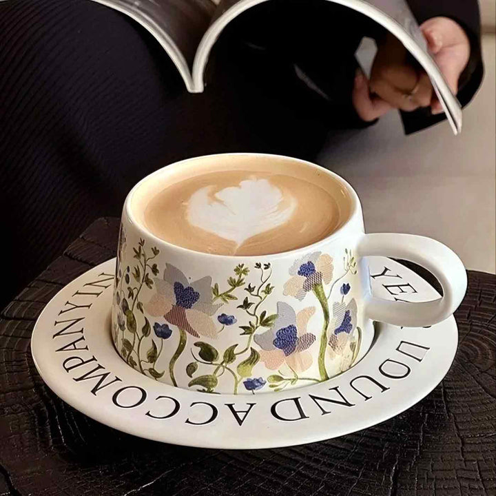 White ceramic cup with latte on desk while woman reads book, elegant coffee table setup