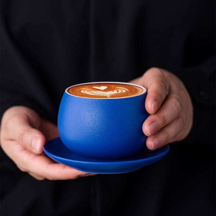 Close-up of woman holding Klein blue ceramic cup with latte art, highlighting elegant refined design